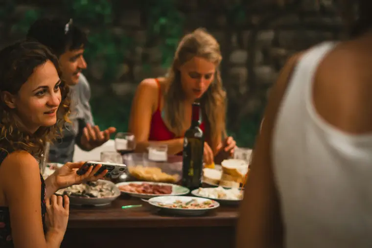 Four people around a table mid-meal, plates and bottles between them, laughing at something off to the side.