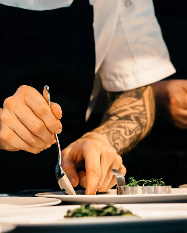 A cook's hands laying herbs onto a plate at the pass.