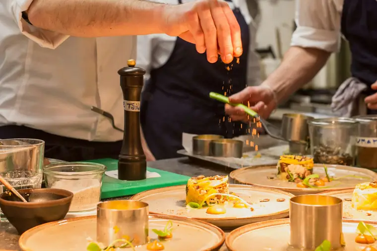 Two cooks working side by side at the pass, seasoning plates under a warm lamp.