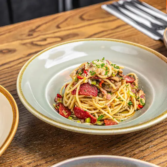 A bowl of pasta in tomato sauce on a worn wooden table, fork resting beside it.